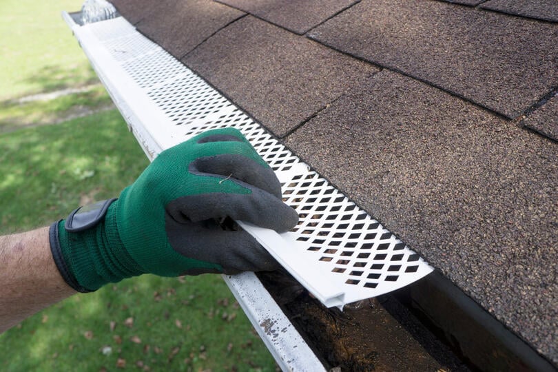 best gutter guards-gloved hand installing white gutter guards on a roof's gutter system