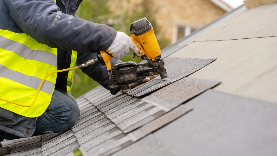 bad roofing contractors-close up view of roofer using a power tool to install roof shingles