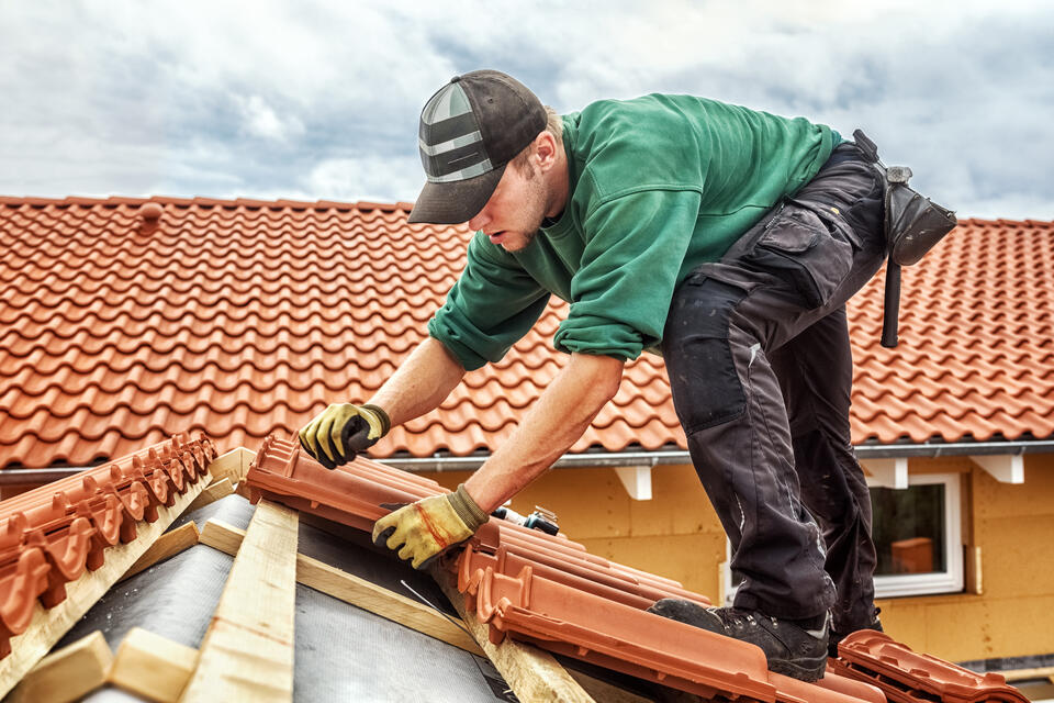 bad roofing contractors-man standing on clay tiled roof installing roofing materials