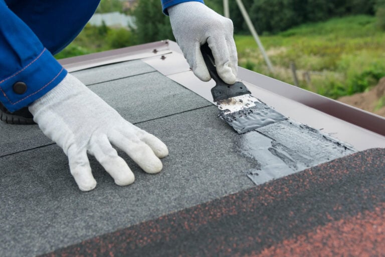 best roof sealant for asphalt shingles-man wearing gloves and blue work suit applying a sealer to roof seams while installing shingles