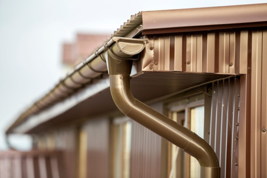 Close-up detail of cottage house corner with metal planks siding and roof with steel gutter rain system. Durability, professional construction, drainage pipes installation and connection concept.