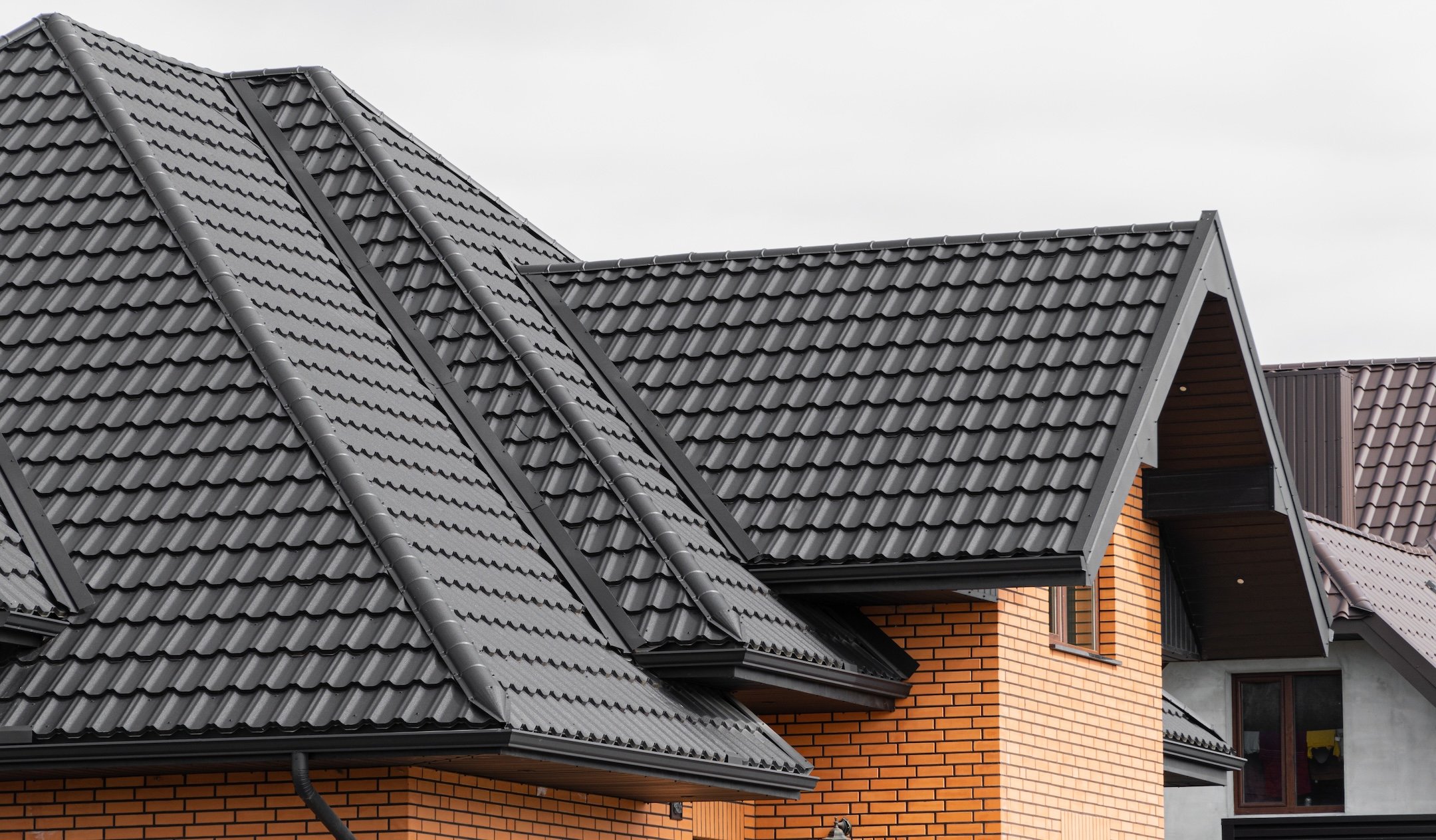 A new house made of yellow bricks and a beautiful black roof. Black corrugated metal profile roof installed on a modern house