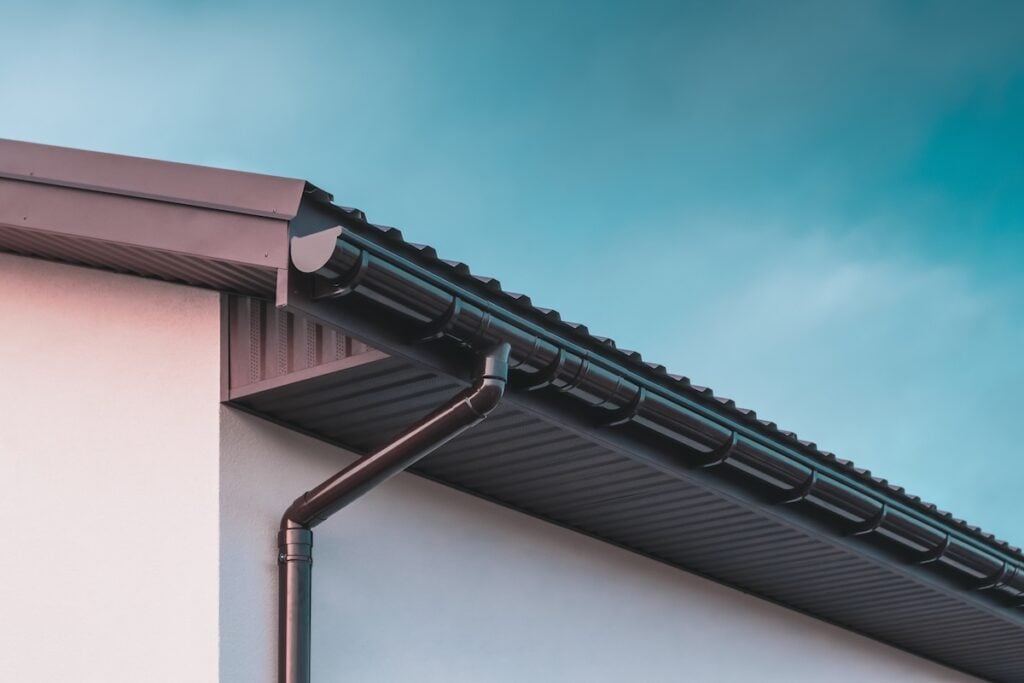 Chocolate-colored plastic gutter on the roof of the building and downpipe on the wall. how to install gutters on a metal roof