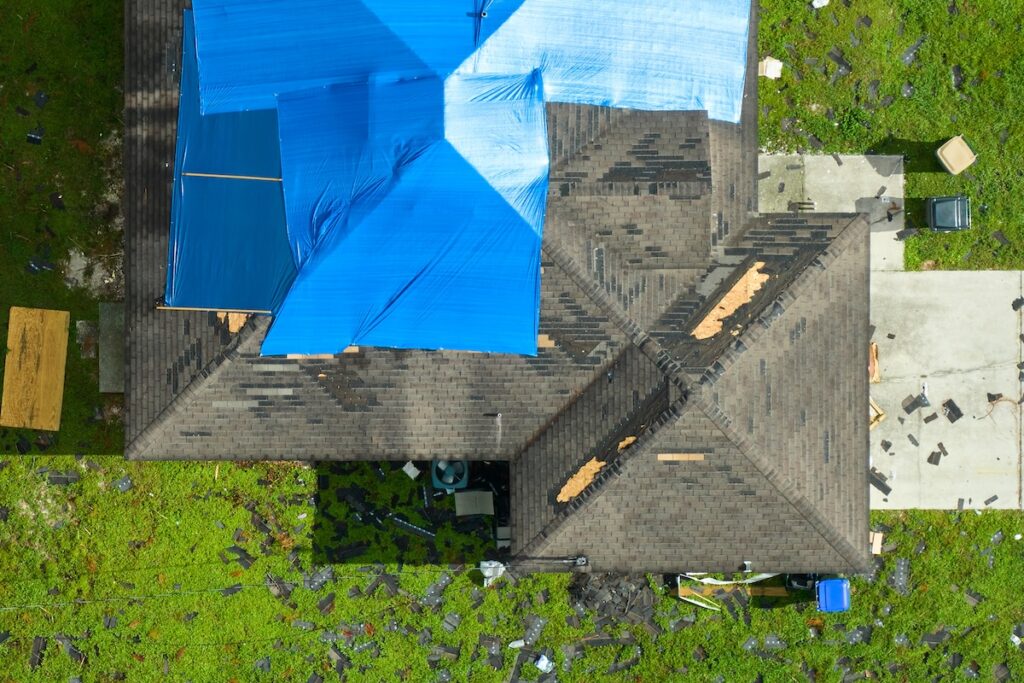 Top view of leaking house roof covered with protective tarp sheets against rain water leaks until replacement of asphalt shingles. Damage of building rooftop as aftermath of hurricane Ian in Florida.
