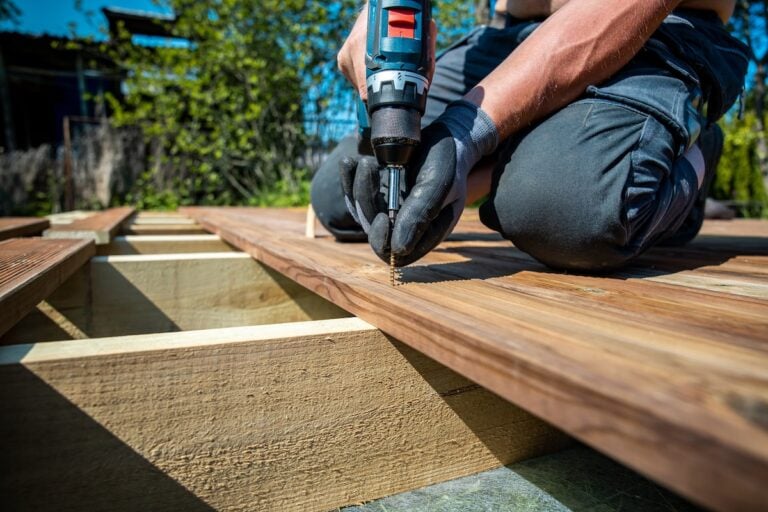 Deck construction, builder hand with electric screwdriver installing impregnated wooden boards