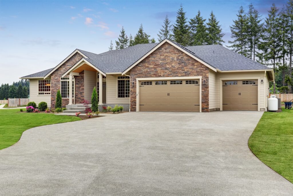 Luxury one level house exterior with brick trim, garage, well kept garden and driveway.