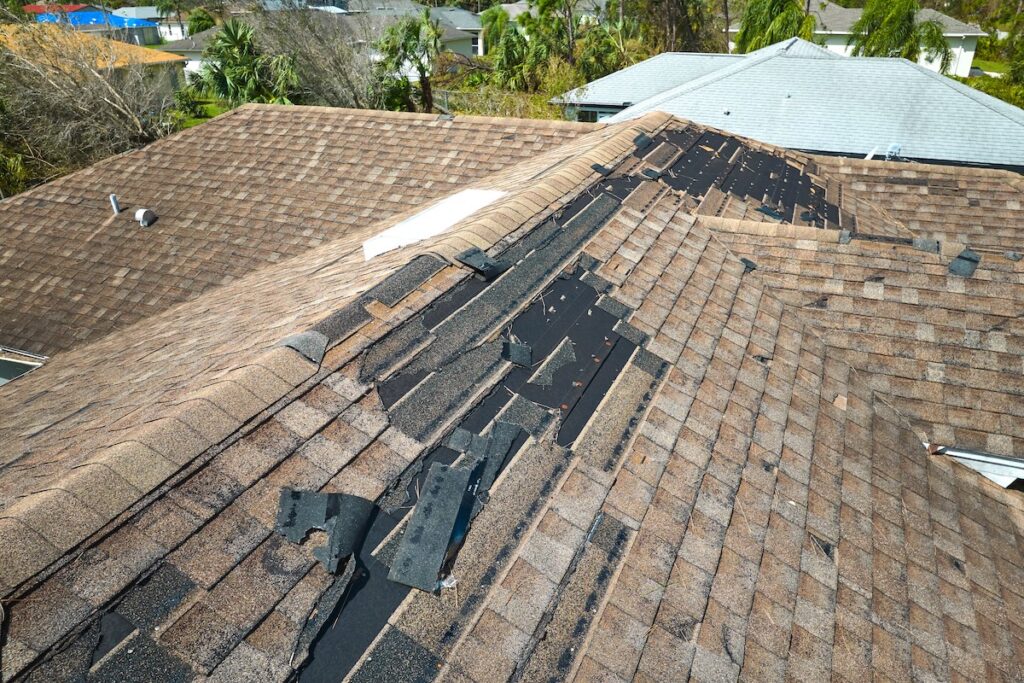Damaged house roof with missing shingles after hurricane Ian in Florida. Consequences of natural disaster.