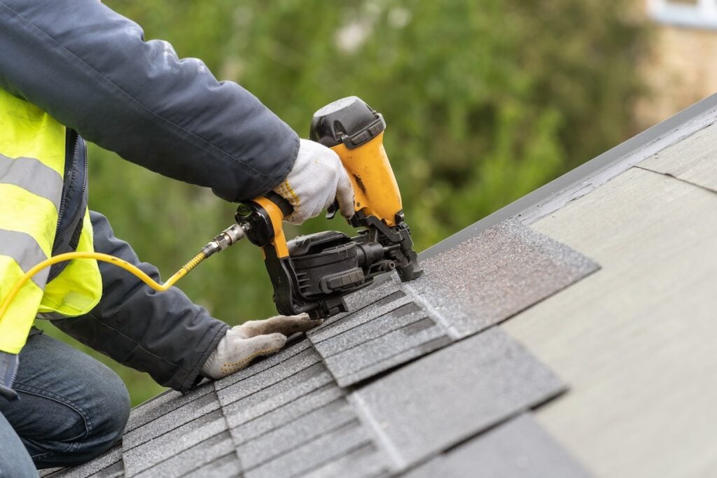 what are starter shingles roofer worker in uniform work wear using air or pneumatic nail gun and installing asphalt or bitumen tile on top of the roof under construction house