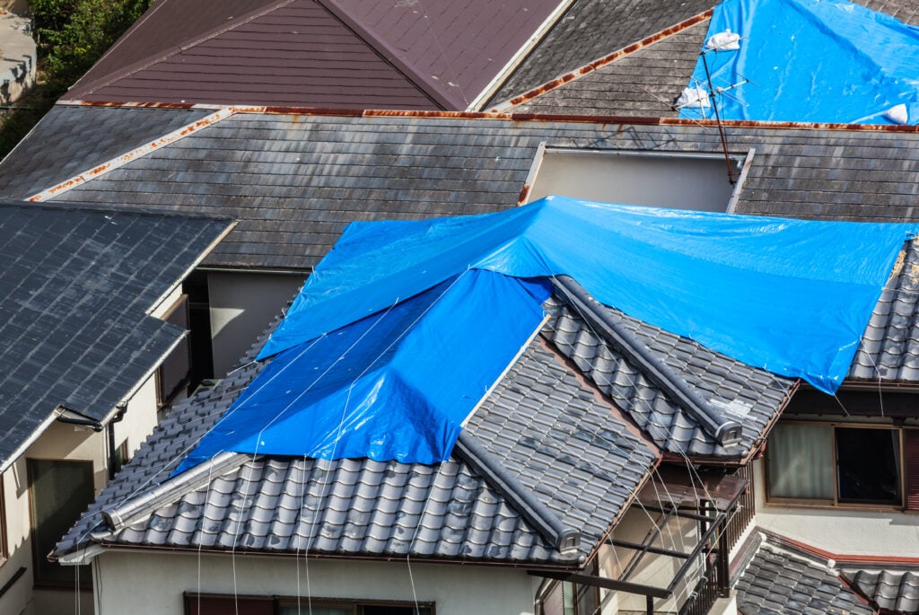 how to put a tarp on a roof without nails High angle view of houses hit by natural disaster, with damaged tiled roof covered with blue tarp