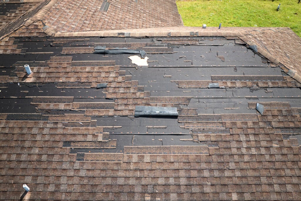 how to dispose of shingles Wind damaged house roof with missing asphalt shingles after hurricane Ian in Florida. Repair of home rooftop concept.