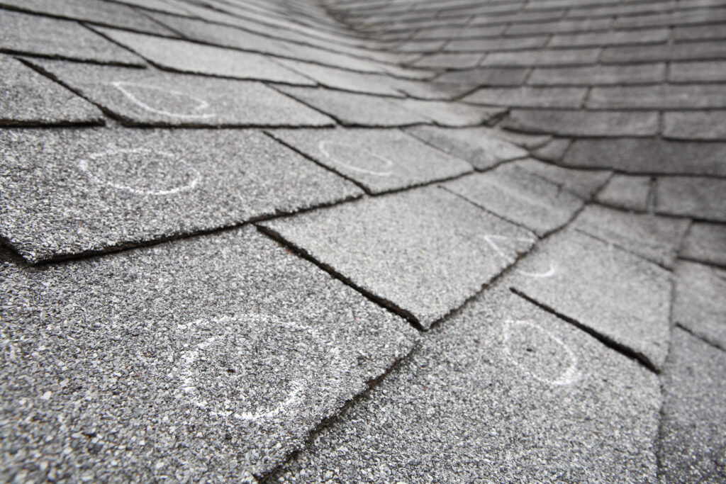 types of roof damage Old roof with hail damaged shingles, chalk circles mark the dama