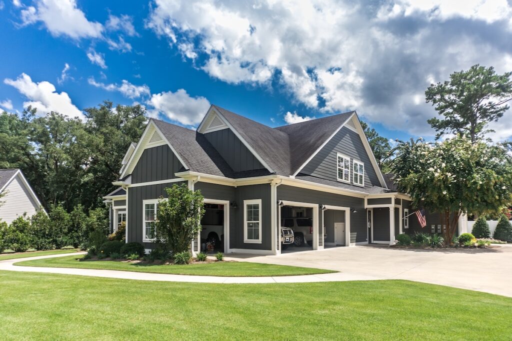roof lifespan The side view of a large gray craftsman new construction house with a landscaped yard a three car garage and driveway.