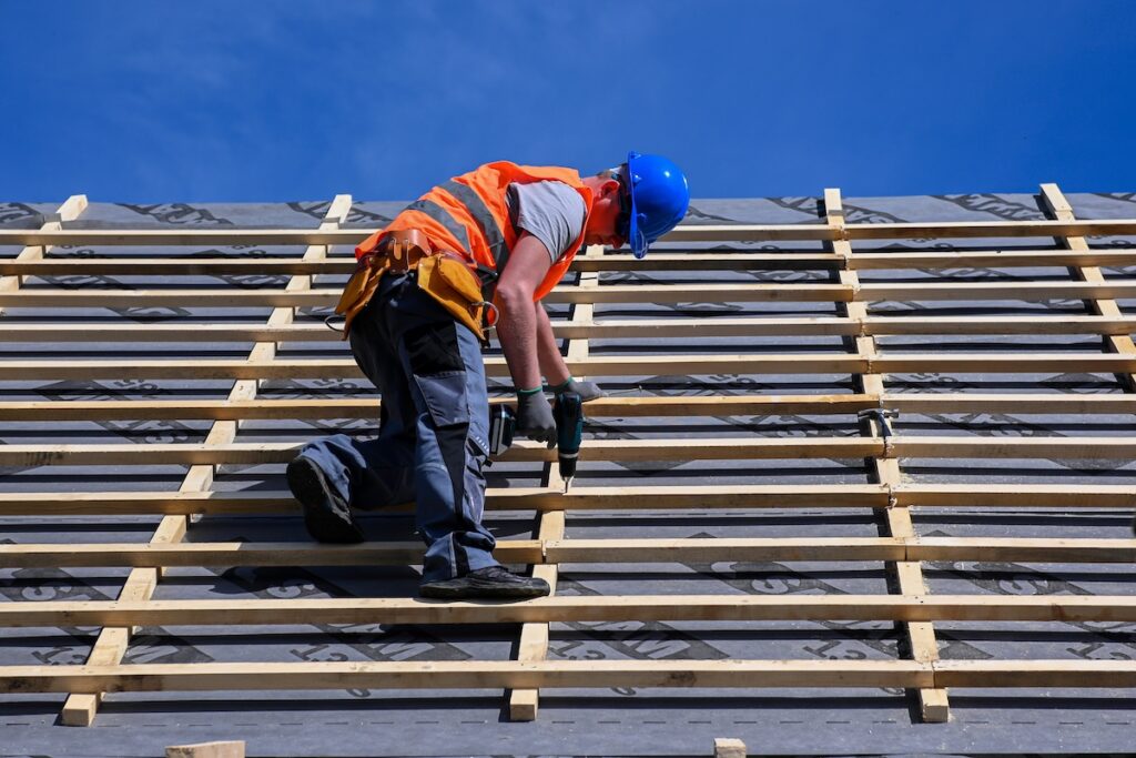 roof upgrade  Repair and replacement of the old roof with a new one. Construction worker in protective clothing standing on roof with tools.