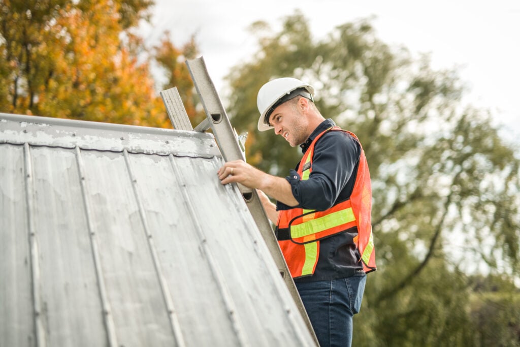 metal roof inspection A man with hard hat standing on steps inspecting house roof