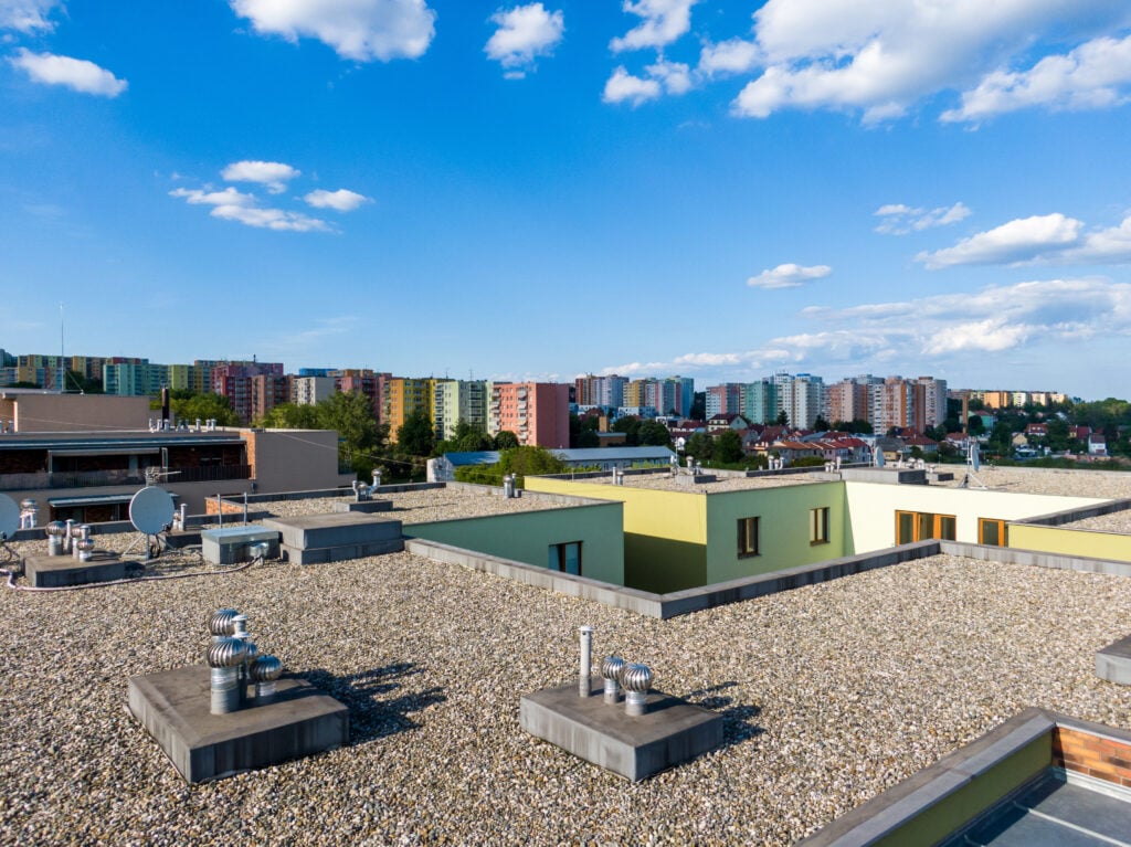 Aerial view of house flat roof on residential building. Modern architecture exterior. Air conditioning systems and ventilation structure. Residential building in background, sunny day.