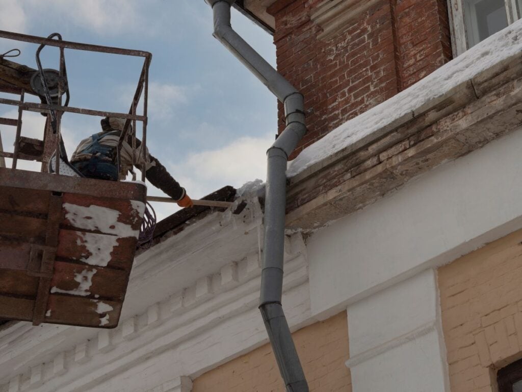 Man, industrial climber on insurance, cleans the roof of a building from snow with a shovel