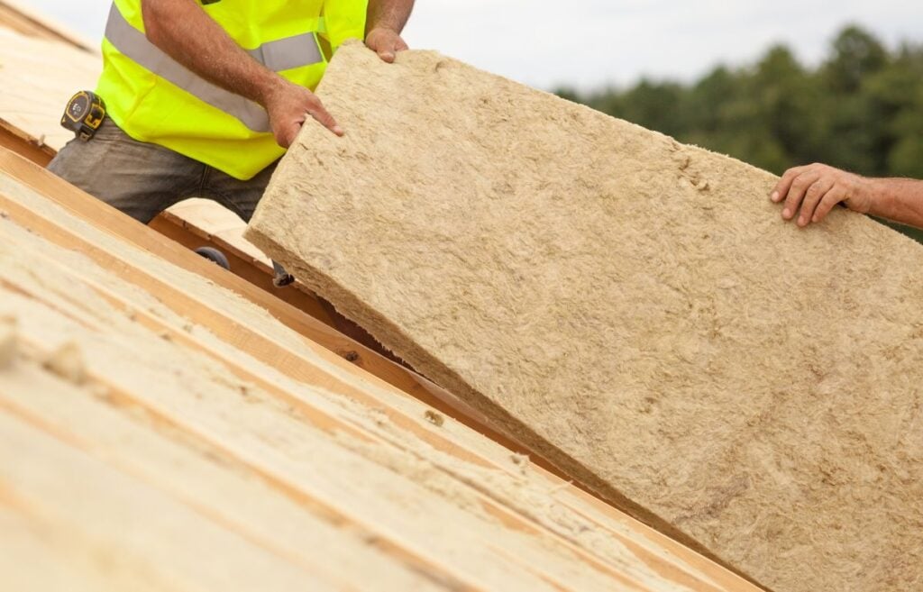 Roofer builder worker installing mineral wool insulation on a roof