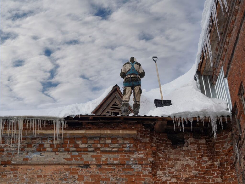 man on a commercial roof clearing snow with a shovel