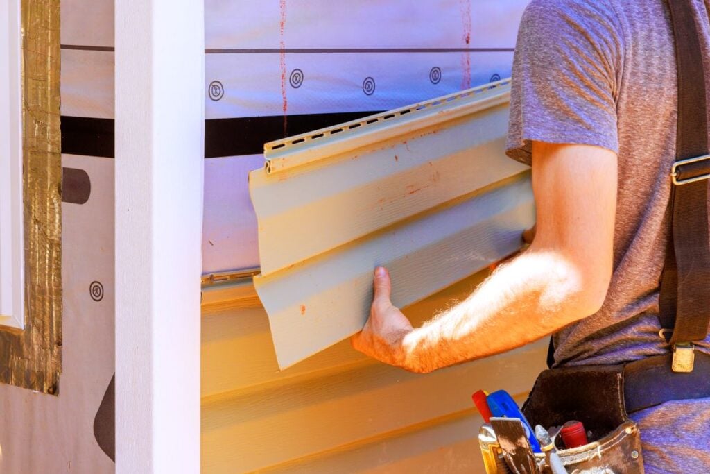 Construction worker installs siding on house during sunny afternoon in residential area