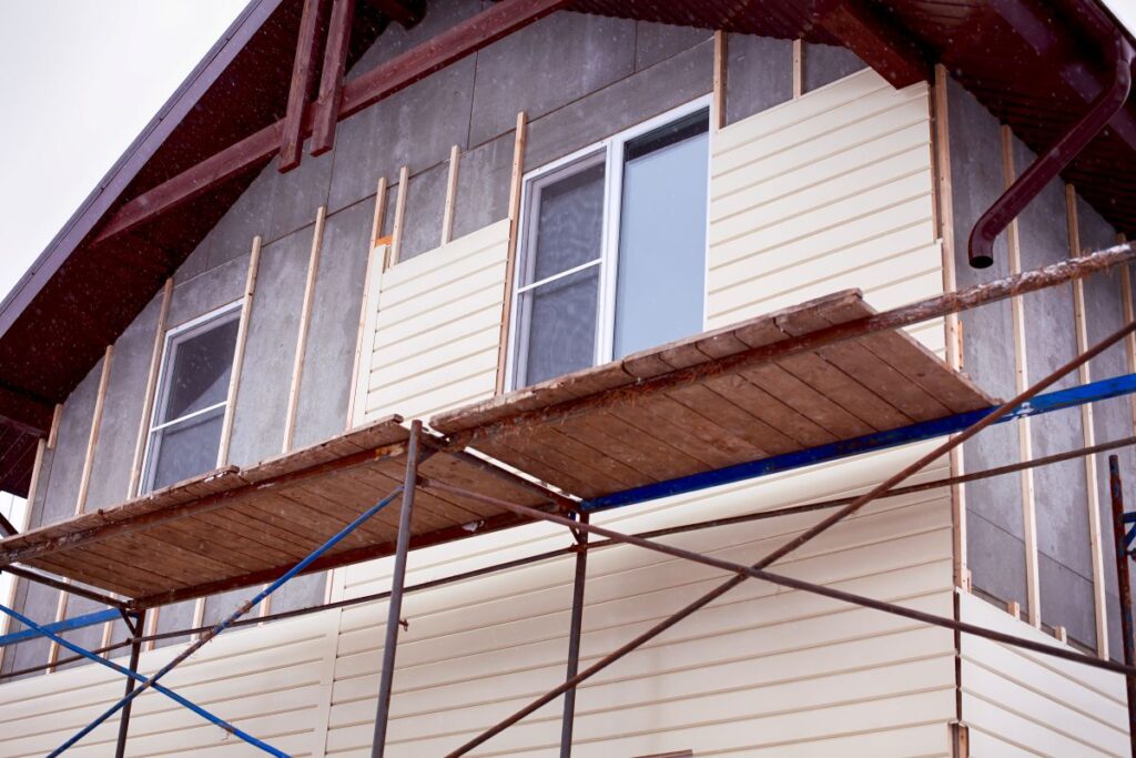 Scaffolding around house with beige siding covering walls